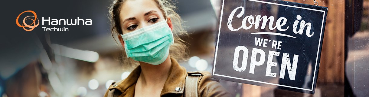A woman wearing a protective face mask walking past a store entrance with a "Come in WE'RE OPEN" sign