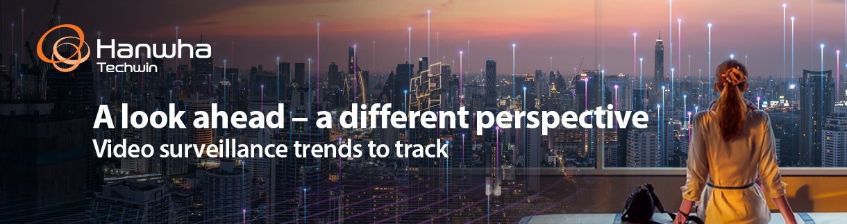 A person looking out a high-rise window at a illuminated smart city skyline with text reading "A look ahead – a different perspective: Video surveillance trends to track" and the Hanwha Techwin logo